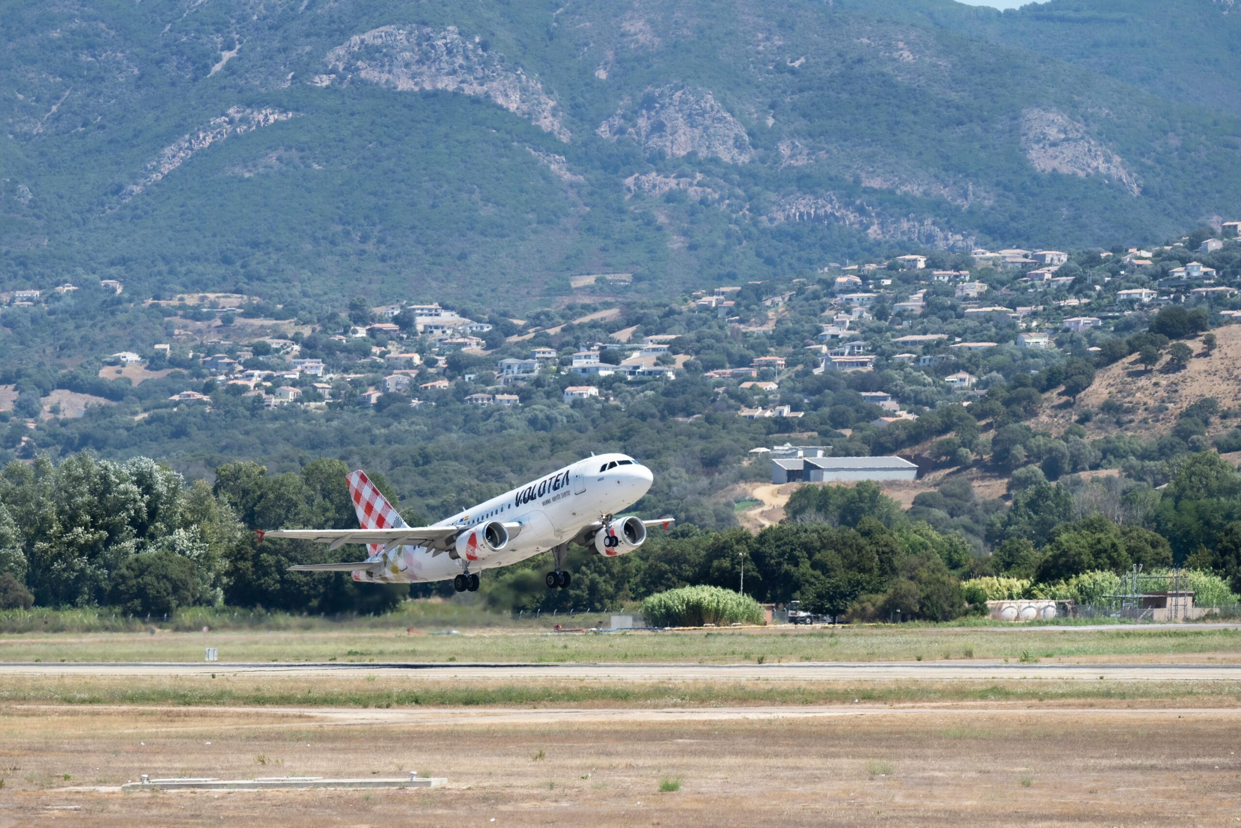 Volotea airline plane taking off at Ajaccio Airport with Corsican mountain backdrop.